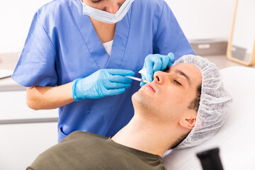 Young man patient of beautician receiving rejuvenating facial injections, concept of male aesthetic...