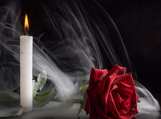 the bright flame of a burning candle illuminates a red rose lying nearby.