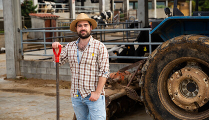 Obraz premium Young man farmer standing near agrimotor during break at cow farm