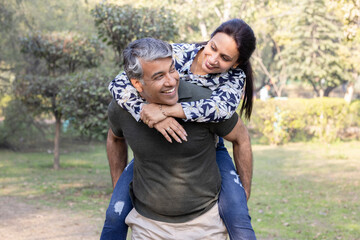 Happy couple enjoying piggyback ride in park