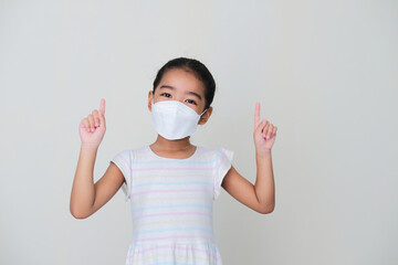 Asian kid wearing medical mask showing happy expression while pointing fingers up
