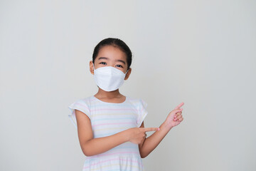 Asian kid wearing medical mask showing happy expression while pointing to the left