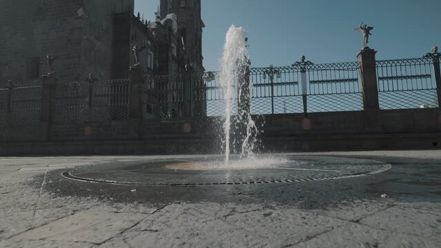 Slow motion dolly shot of splashing fountain on road in front of holy Puebla Cathedral in Mexico 