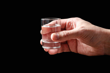 A glass of vodka in a man's hand. Black background. Copy space