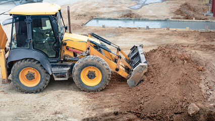 A multipurpose excavator with a front bucket transports soil to the construction site. View from above. Construction machinery for earthworks.