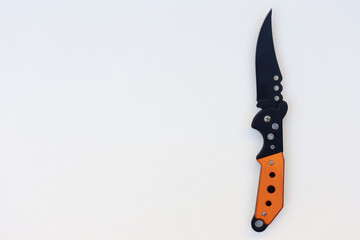 Isolated designer black knife with orange handle. Isolated knife with textured white background. knife on paper