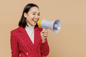 Smiling happy woman of Asian ethnicity 20s wear red jacket hold scream in megaphone announces discounts sale Hurry up isolated on plain pastel beige background studio People lifestyle fashion concept.