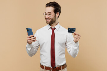 Young employee business man corporate lawyer in white shirt red tie glasses work in office using mobile cell phone credit bank card shopping online order delivery isolated on plain beige background.