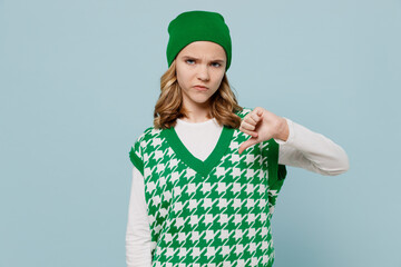 Frowning distempered sad young brunette girl teen student wears checkered green vest hat look camera showing thumb down dislike gesture isolated on plain pastel light blue background studio portrait.