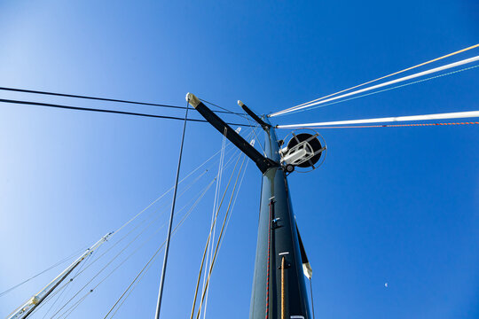 The mast of a sailing yacht with a radar, sail ropes and a folded sail, viewed from below against the sky.