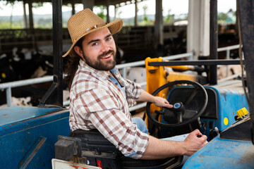 Portrait of smiling young bearded farmer sitting on small farm tractor..