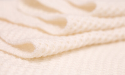 Fototapeta na wymiar Knitted surface of woolen things as a background. Close-up of soft white texture of knitted patterns. Warm winter clothes. Background textile surface with copy space for text.
