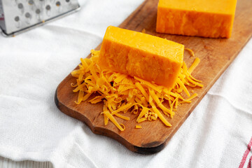 Shredded Sharp Cheddar Cheese on a rustic wooden board, side view.