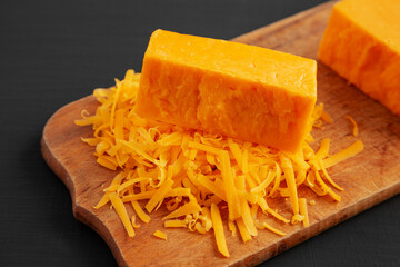 Shredded Sharp Cheddar Cheese on a rustic wooden board on a black background, side view.
