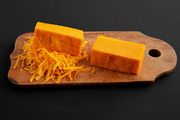 Shredded Sharp Cheddar Cheese on a rustic wooden board on a black surface, side view.