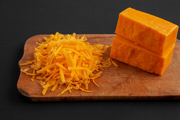 Shredded Sharp Cheddar Cheese on a rustic wooden board on a black surface, side view.