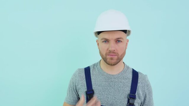 General worker in a helmet and overalls yawns on a blue background