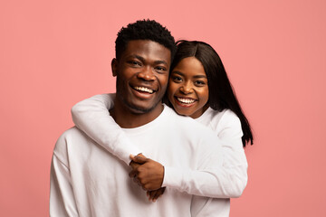 Happy black couple cuddling on pink studio background