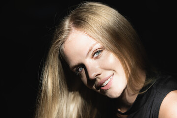 Blonde girl close up face. Portrait of elegant woman with light on a black background. Beautiful female face in the darkness.