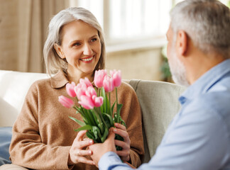 Happy senior woman getting romantic present bouquet of tulips from loving husband on Valentine's Day