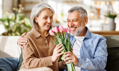 Happy senior woman getting romantic present bouquet of tulips from loving husband on Valentine's Day