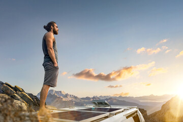 Man standing on the roof of his camper van parked in the mountains