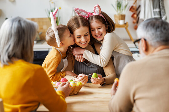 Cute little children embracing and kissing young happy mother while painting Easter eggs with family