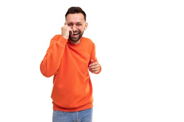 a man in an orange sweater laughs holding his hands to his stomach and face on a white background