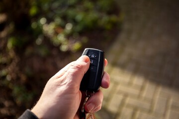 A close-up portrait of a hand of a person holding a car key pressing the unlock button with the thum. The remote control has unlock, lock and a trunk icon on it.