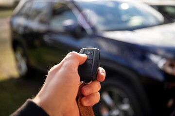A close up portrait of a person standing next to a car holding a car key in his hand pressing the unlock button. the remote control has unlock, lock icons for the doors and the trunk of the vehicle.