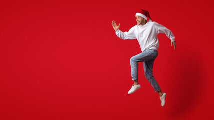 Christmas Rush. Excited Young Man In Santa Hat Jumping On Red Background