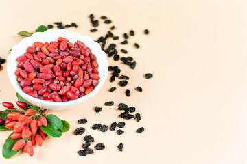 Fresh red and dried barberry berries with green leaves in a white bowl on a yellow background. Space for text.