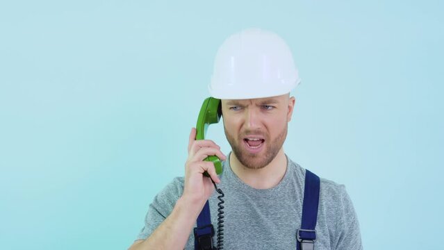 Serviceman in overalls and helmet speaks on an old telephone and consults a client on a blue background