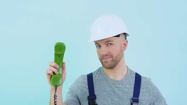 Repairman in overalls and helmet holds an old phone in his hands and points to it