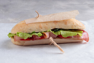 Close-up view of the banh mi sandwich with sliced grilled pork and peppers and salad packed in paper on white paper. Selective focus.