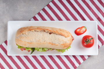 Top view of the banh mi sandwich with sliced grilled pork and peppers and salad packed in paper on white plate. Selective focus.