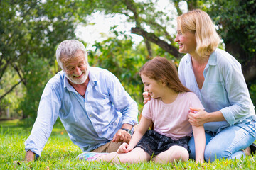 happy family elderly caucasian and child caucasian sitting on lawn relax in weekend holiday lifestyle in park .