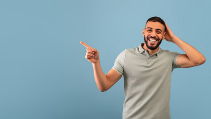 Fototapeta premium Look at this offer. Excited arab man pointing aside showing empty space for your text or ad, blue background