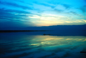 Mountains and clouds reflected in perfect symmetry in the Dead Sea in the early morning blue light at sunrise.