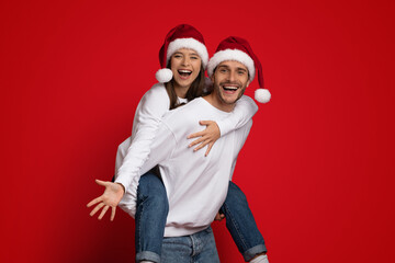 Xmas Mood. Cheerful Couple Wearing Santa Hats Having Fun On Red Background