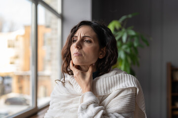 Upset sick woman standing at home touching swollen glands, having pain or scratchy sensation in throat, selective focus. Female suffering from angina or tonsillitis caused by infection or irritation