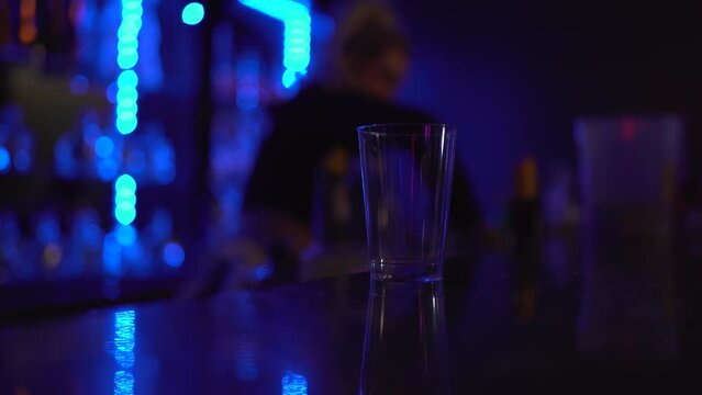 An empty Glass sits on a bar while the bartender is busy with other tasks