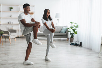 Young black couple doing high knee exercise at home
