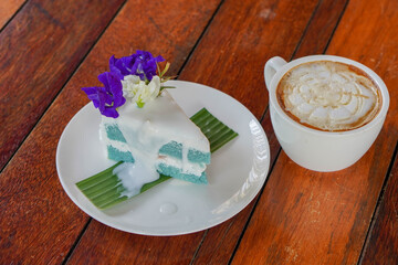 top view Coconut Cake on green banana leaf on white ceramic plate and coffee in white ceramic mug, on wooden floor background, food, dessert, copy space