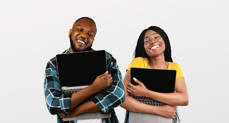 Technology Lovers. Happy black man and woman hugging laptops with blank screen