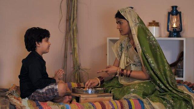 A cheerful village mother feeding her cute son delicious homemade food - healthy food  love and care  parenting . A young child throwing tantrums while eating food - domestic lifestyle