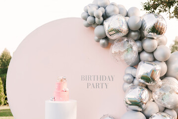 A large pink cake with a pink photo zone of silver balloons on the background. Party decorated with balloons