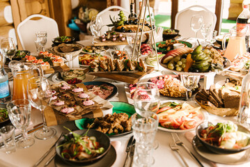 Beautifully decorated catering banquet table with different food snacks and appetizers with sandwich, caviar, fresh fruits on corporate party event or wedding celebration