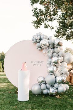 A large pink cake with a pink photo zone of silver balloons on the background. Party decorated with balloons
