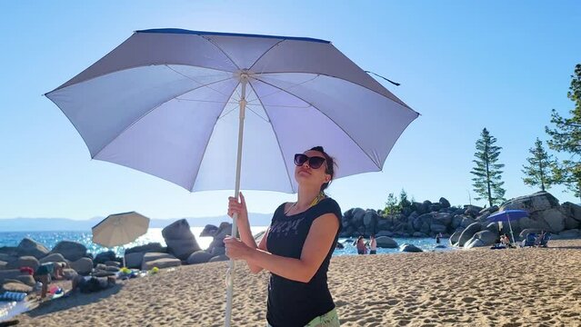 Woman Spinning Umbrella In Sunglasses Standing At The Beach On A Sunny Day In Lake Tahoe, USA. - medium shot